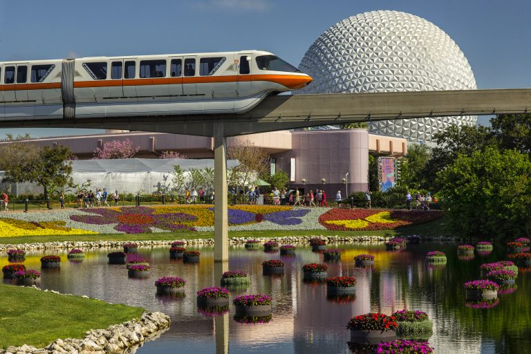 A monorail trails past the Epcot ball during the arts festival: stunning colors of flowers are seen below the line of the monorail. 