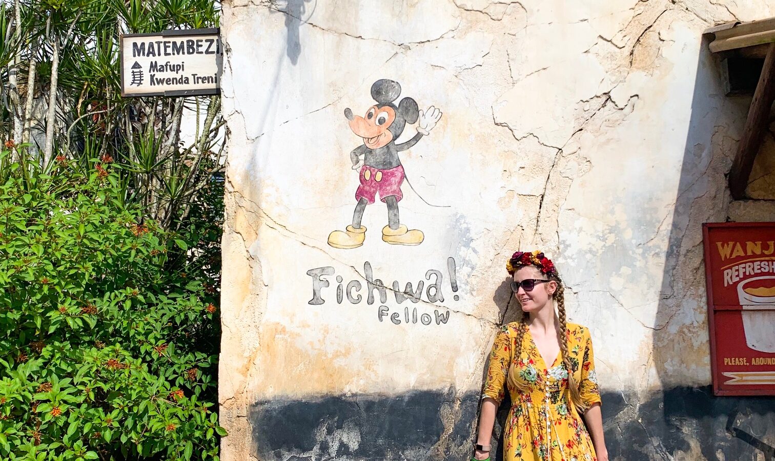 A woman in a yellow, floral dress by a Mickey mural, enjoying Animal Kingdom for adults.
