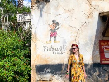 A woman in a yellow, floral dress by a Mickey mural, enjoying Animal Kingdom for adults.