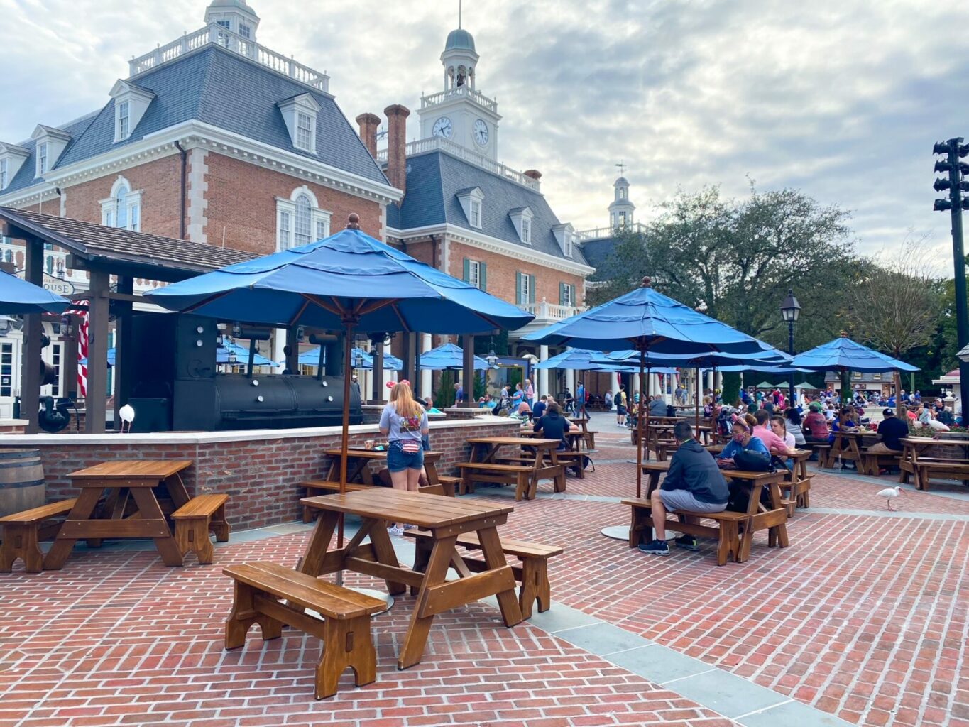 blue umbrellas over picnic tables in front of colonial style brick building 