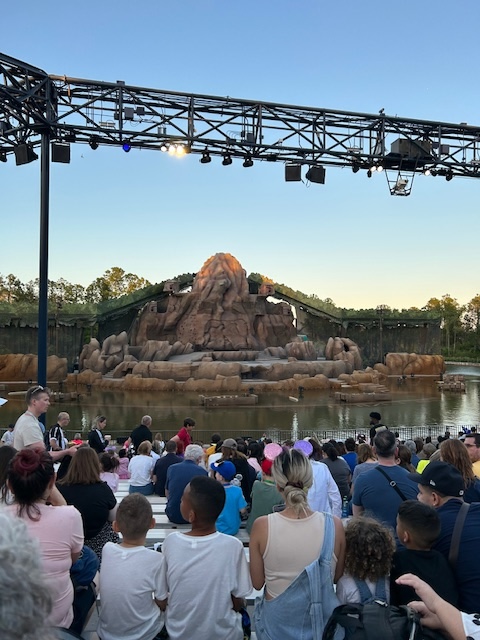 large rock formation in front of water and an audience under a black light strip 