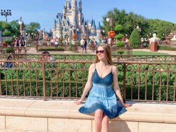 woman sitting in blue sundress with the castle at magic kingdom in the background