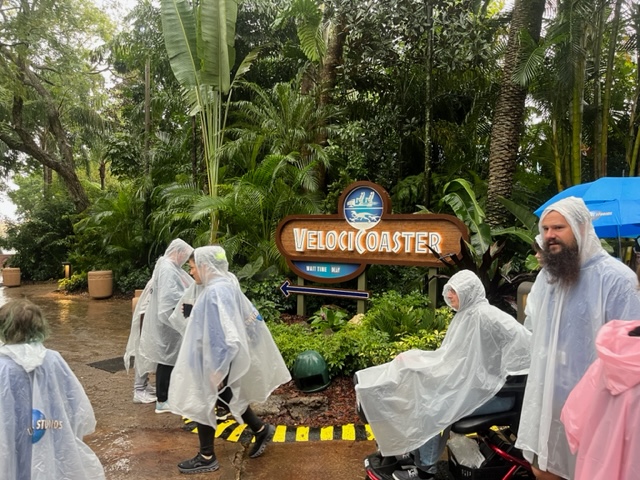 Guests in ponchos walk by the a giant coaster, trying to stay dry in the rain, but still enjoying Universal Orlando in the rain!