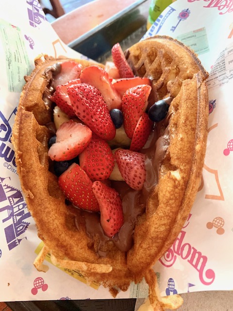 waffle sandwich with fresh strawberries piled into the middle on a piece of paper magic kingdom breakfast