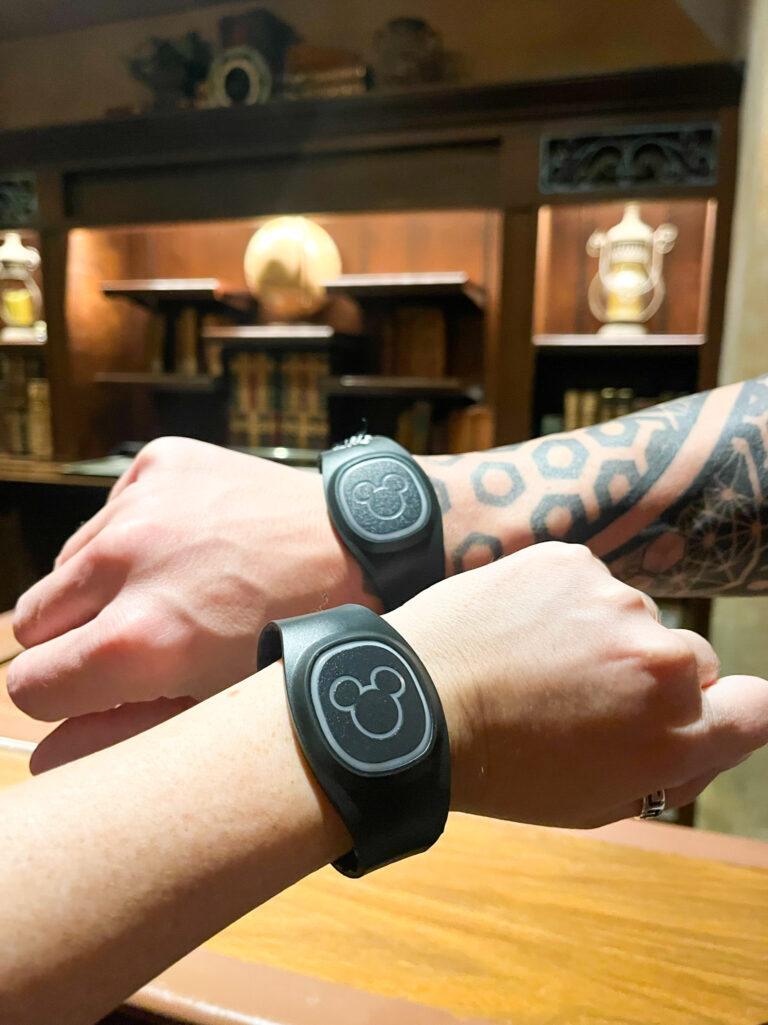 Two people hold up their wrists for a photo of their Magicbands, which are black in color and feature the mickey ears.