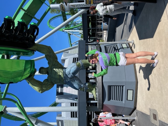 A woman in a Incredible Hulk shirt stands with her arms up in front of the Incredible Hulk Coaster, ready to do the single rider line because she knew what mistakes to avoid at Universal Orlando, and was willing to ride alone for a shorter wait time.
