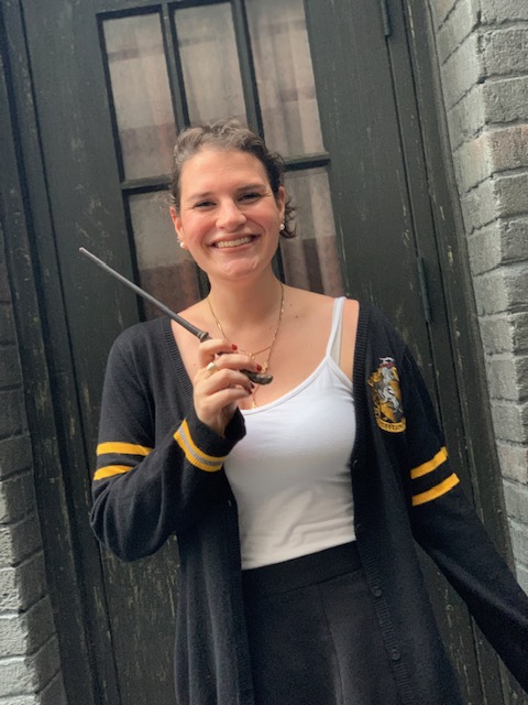 A woman in a Hufflepuff sweater stands in front of Olliveanders with her personalized, interactive wand. 