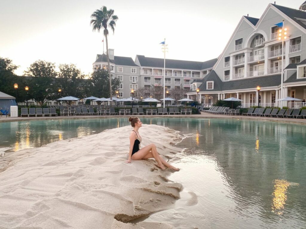 A girl in a black swimsuit sits on the sandbar at one of the Disney property resorts, enjoying early check in: one month before Disney you should check in to make your life easier! 