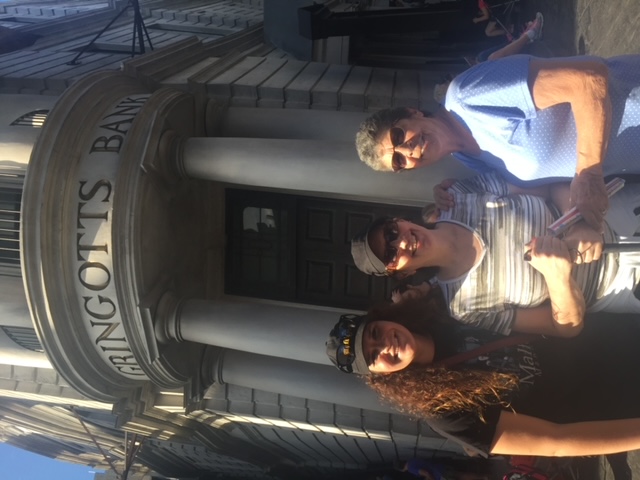 Three generations stand in front of Gringotts Bank, waiting to go on the ride before exchanging money for fancy wizarding money.