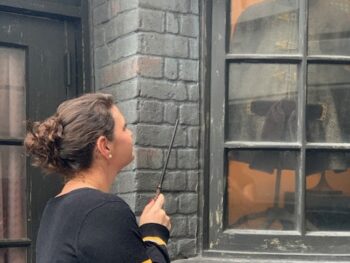 A girl stands in front of a window in Diagon Alley with her interactive wand, looking for one of the Universal Orlando secrets: a special interaction spot not located on a map!