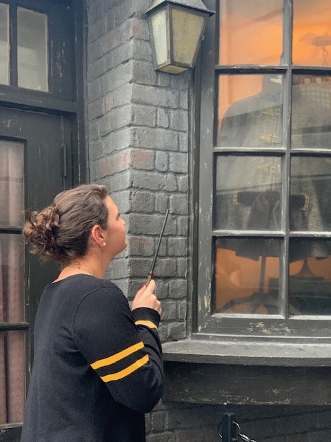 A girl stands in front of a window in Diagon Alley with her interactive wand, looking for one of the Universal Orlando secrets: a special interaction spot not located on a map!
