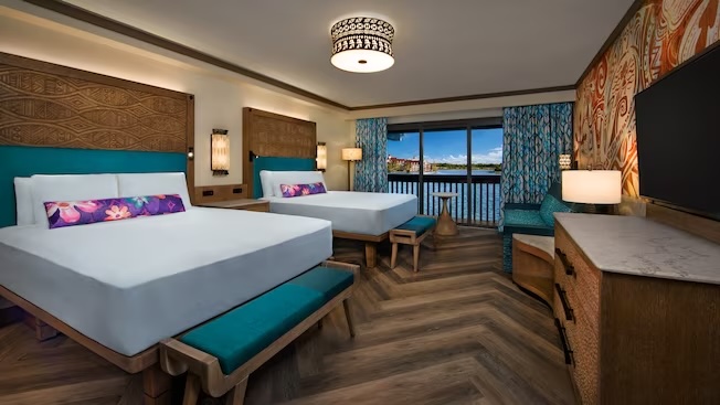 bed with wooden floor and colorful floral pillows and window that overlooks a lagoon