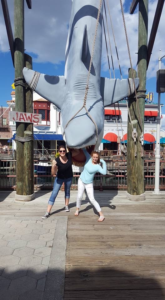 A girl and her friend pose in front of the shark that hangs as a tribute to Jaws: they opt out of paying for photo passes and just asked someone to take a photo to save money at Universal Orlando.