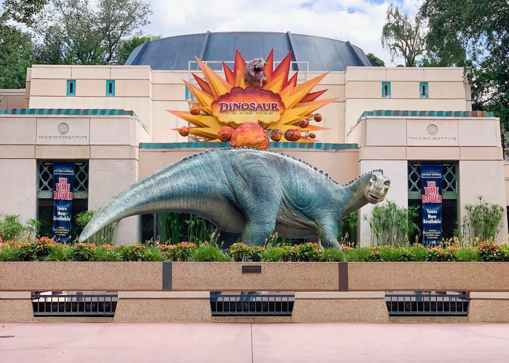 giant green dinosaur statue in front of a beige building and flowers changes for Disney World in 2025 