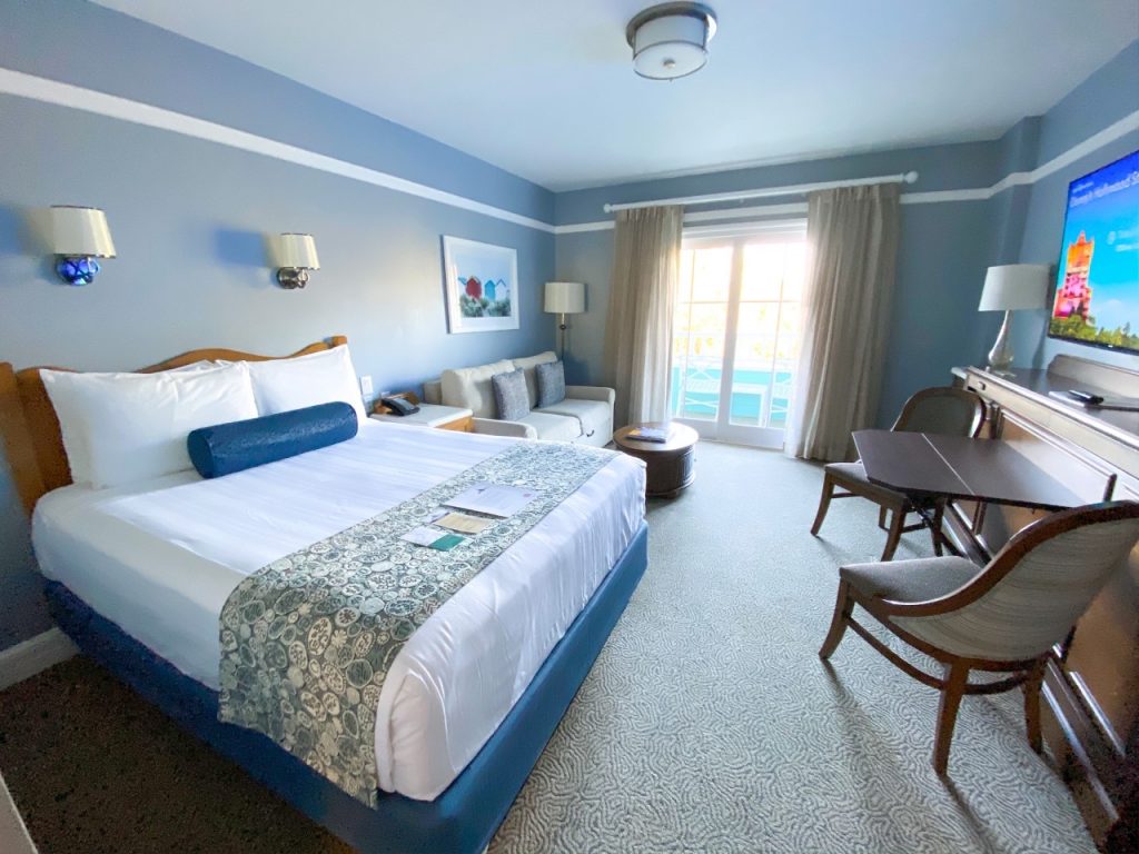 blue and white bed in hotel room with beige carpet, blue walls, and a table and chair set