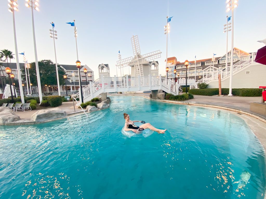 woman in inner tube in large blue pool with white and gray buildings behind her 