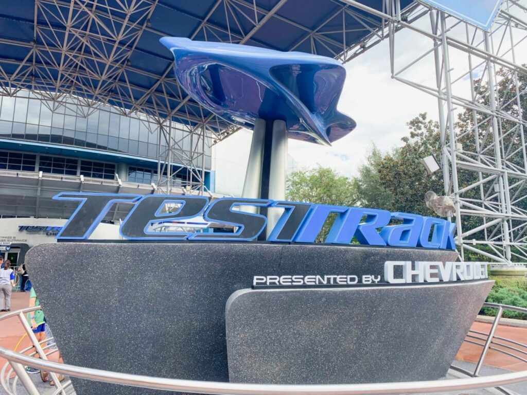 blue and black sign that reads test track in front of metal scaffolding changes to Disney World in 2025