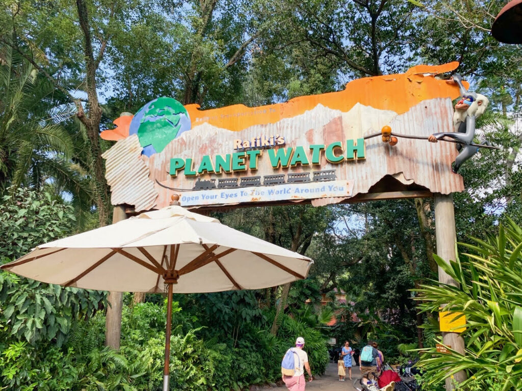 colorful sign for train at animal kingdom behind a tan umbrella 