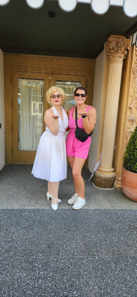 A women in a pink out fit smiles and poses with the character actor of Marylin Monroe, enjoying the shade and break from the heat. They probably would have enjoyed misting fans, which is on our list of things to buy from amazon for Universal Studios. 