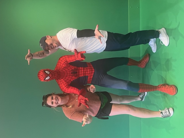 A women and a man stand, posed with Spiderman on a green screen. They didn't' get his autograph but they could have! 