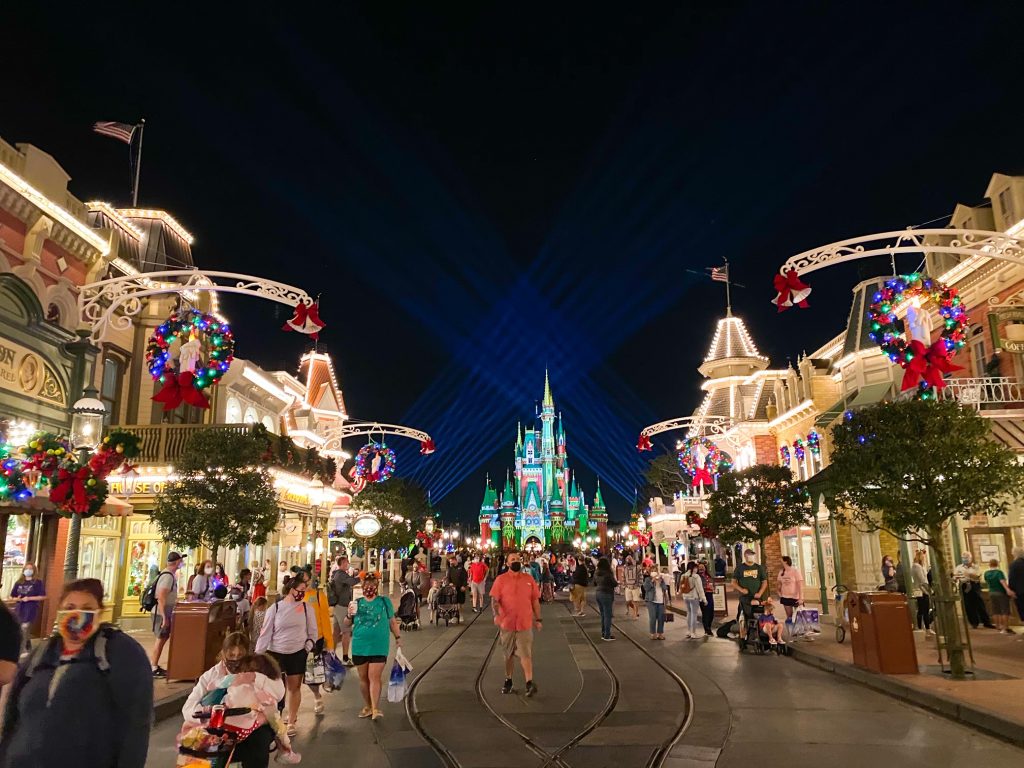 people walking on Main Street in magic kingdom with holiday lights and a green and red castle