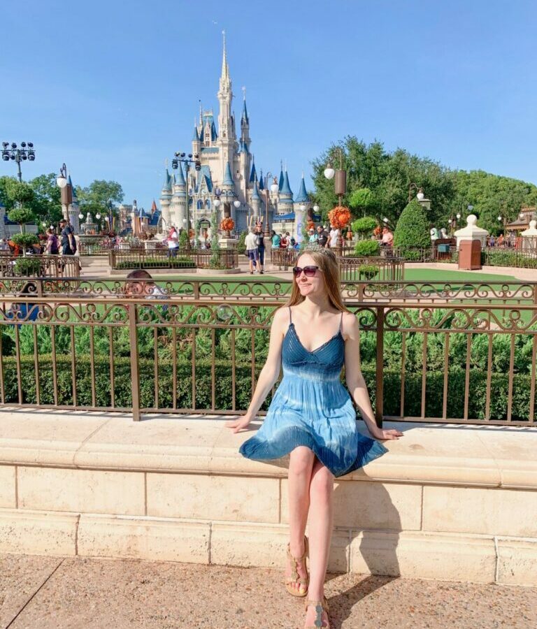 woman in blue dress sitting in front of cinderella castle what to wear in disney in spring