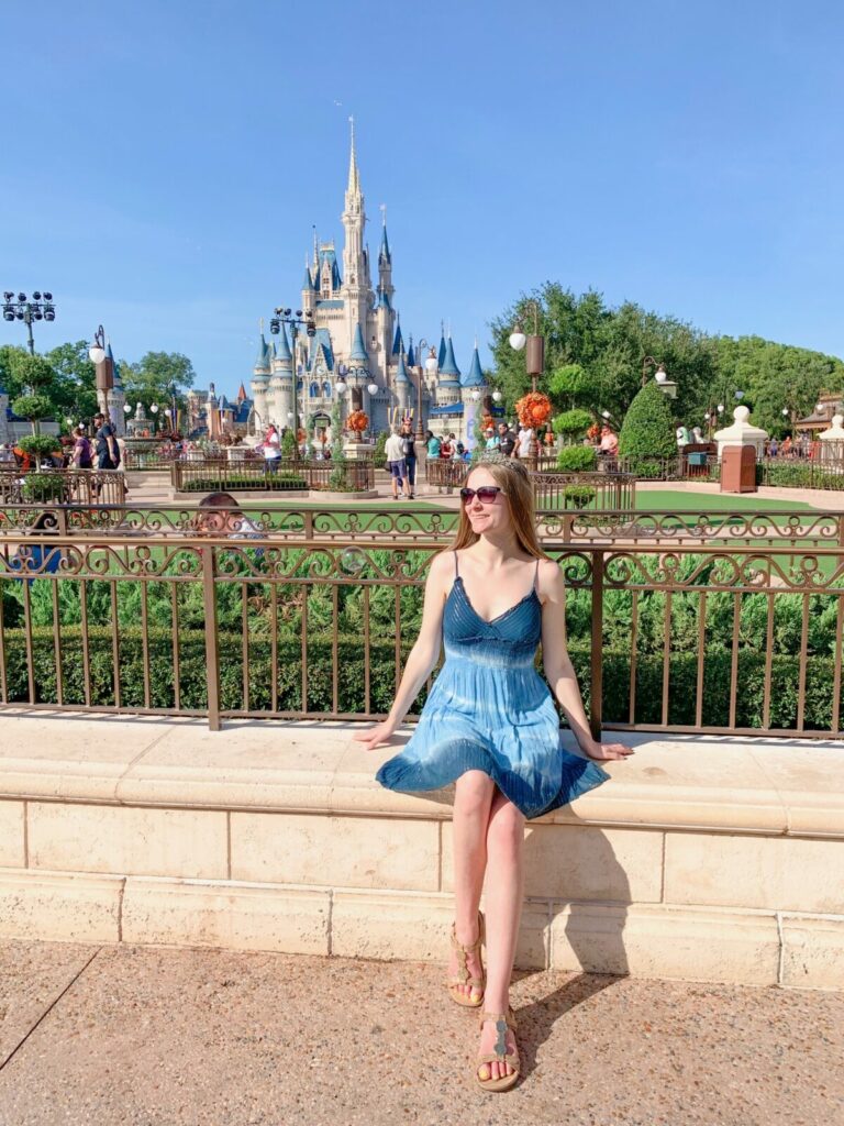 woman in blue dress sitting in front of cinderella castle what to wear in disney in spring