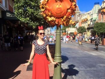 woman in red skirt and black polka dot top near orange Mickey Mouse pumpkin decoration