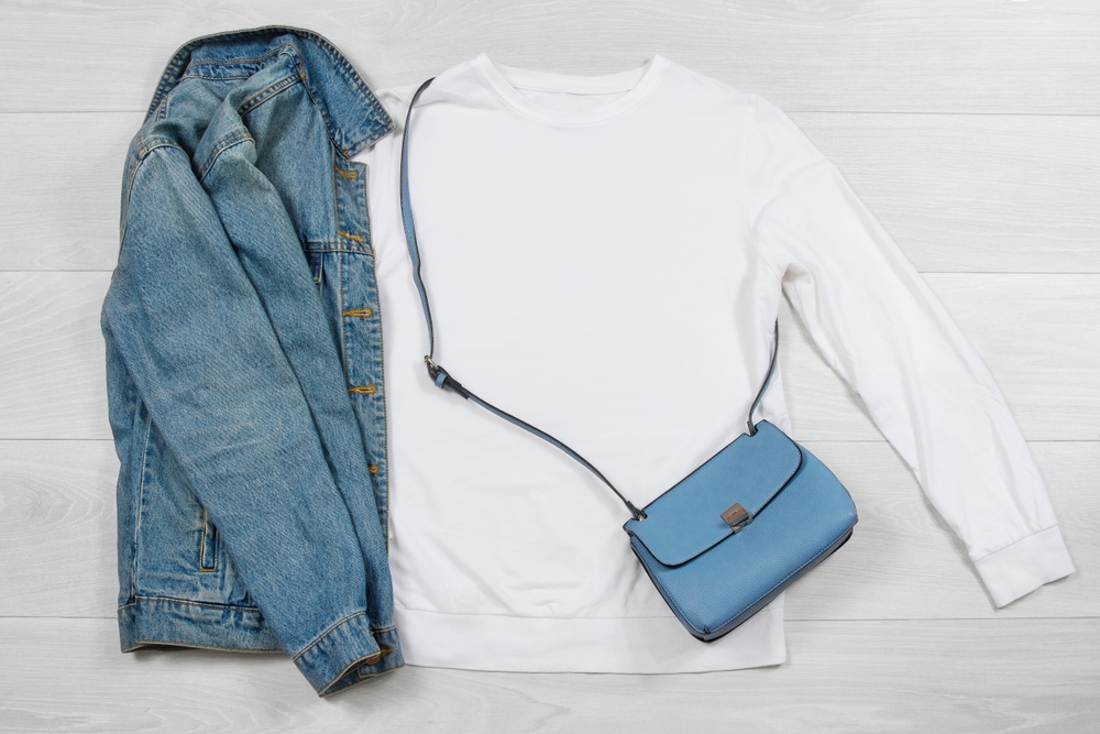 flatlay of white sweatshirt and jean jacket with blue purse what to wear in Disney in fall 