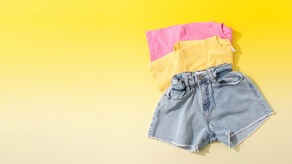 flatlay of kids tees and jean shorts on yellow background what to wear in disney in fall