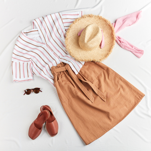 striped white shirt with brown linen skirt and straw hat with brown sandals flatlay on white background what to wear in disney in summer 