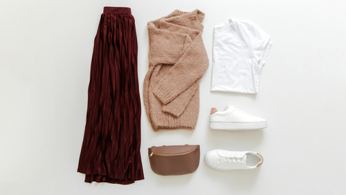 flatlay of white tee, burgundy skirt, tan purse and sweater and white sneakers what to wear in disney in fall 