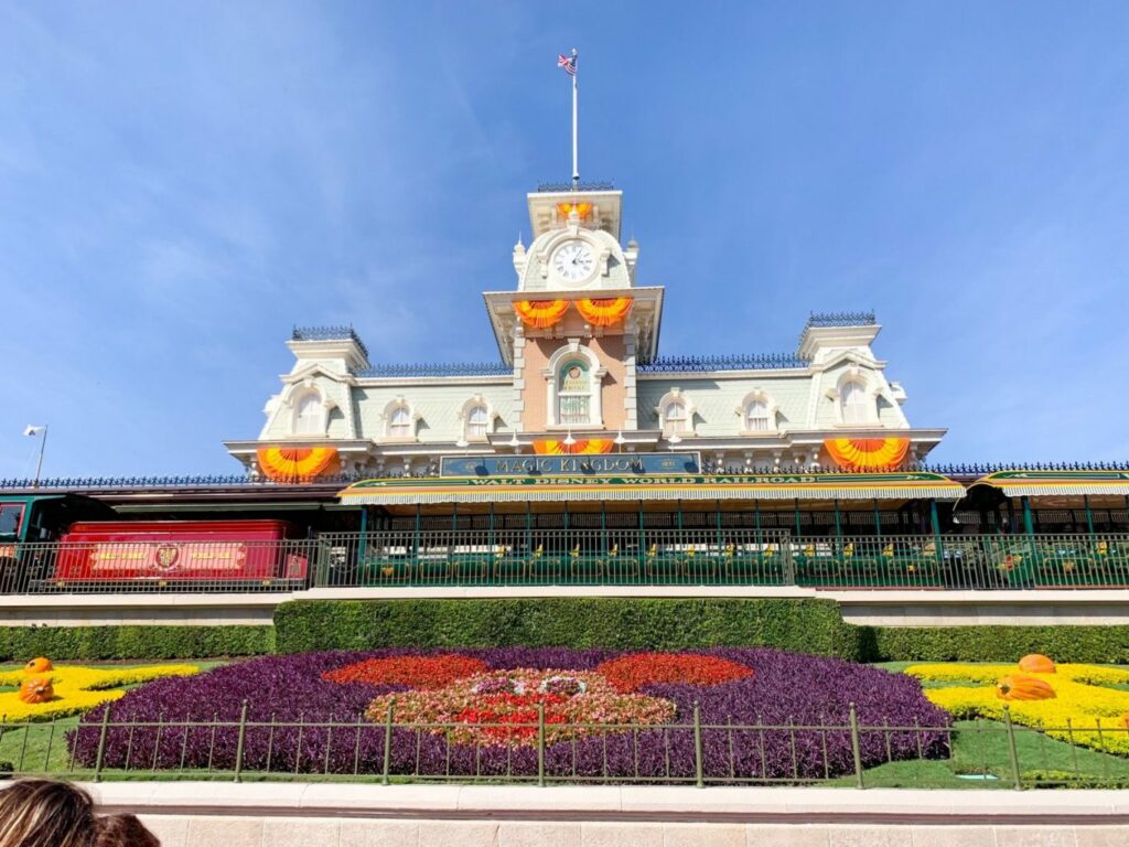 large white train station decorated with orange bunting behind mickey shaped flower display 