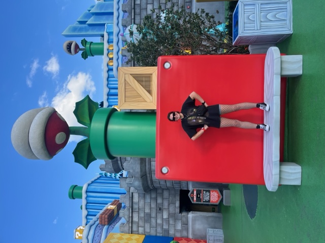 A girl in a black shirt and converse stands on a bench in Nintendo world, her arms on her hips.