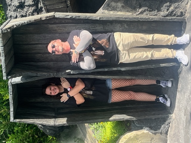 A couple stands in the open coffins in Dark Universe, arms over their chests.