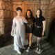 two women in black shorts and tshirts standing next to a employee dressed in costume wearing a white dress and black wig at Epic Universe in Orlando