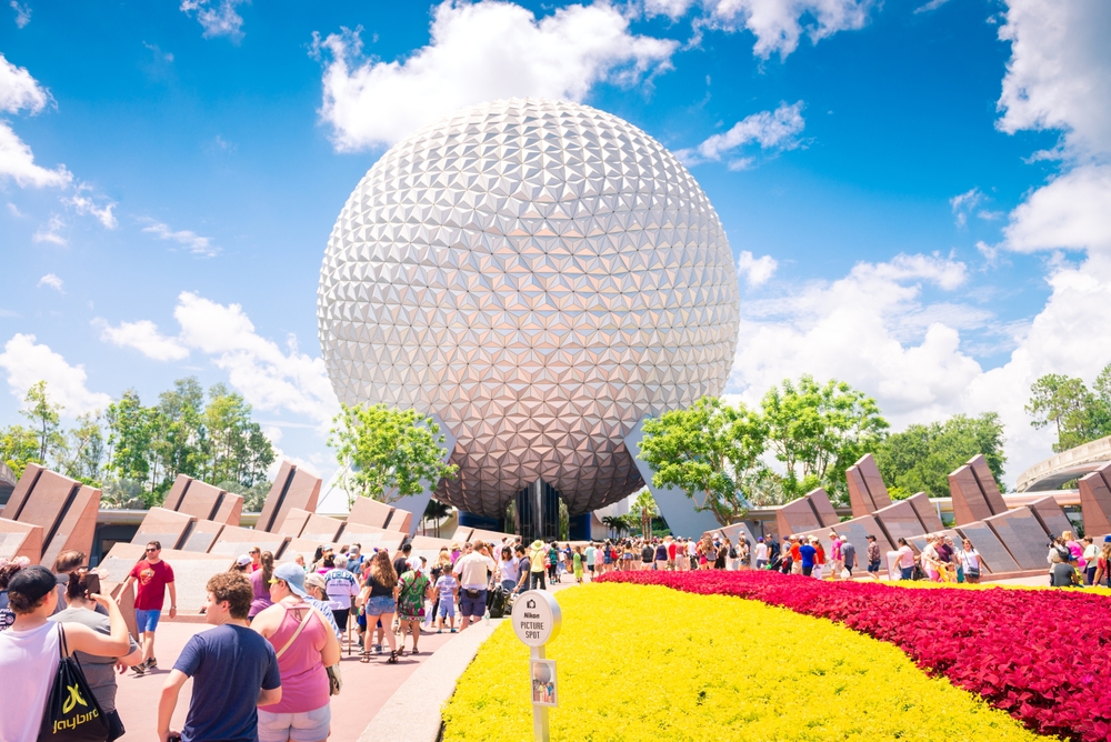A shot of the Epcot ball during a festival shows bright flowers, blue skies, and tourists! 