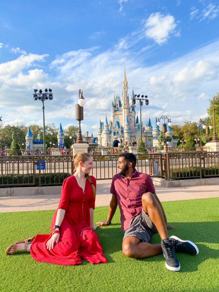 man and woman sitting on grass facing each other in front of fairytale castle disney world picnic spots