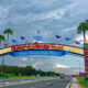 large colorful Walt Disney World sign over road with trees and cloudy sky. there is a road in the foreground going under the sign