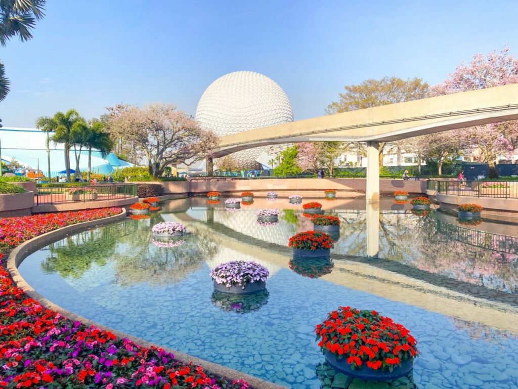 scenic shot of white geodesic sphere over a monorail track and flowers and a water feature 